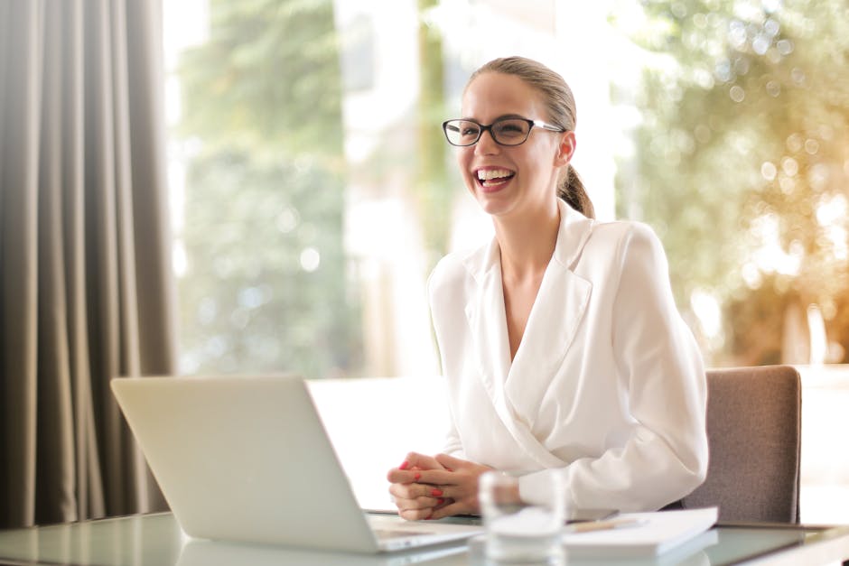 Cheerful businesswoman in glasses working on a laptop, in a bright and modern office setting