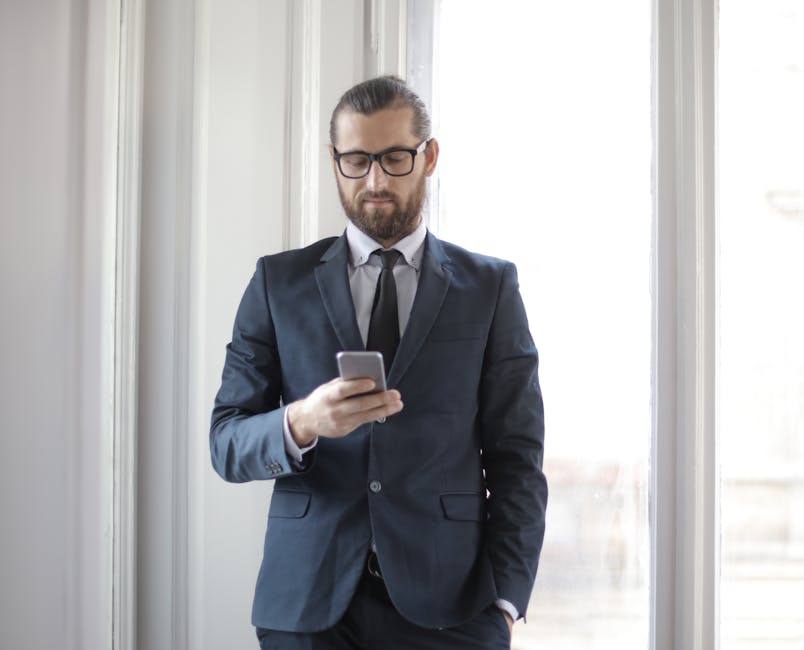 Confident man in formal suit using smartphone by window in office setting